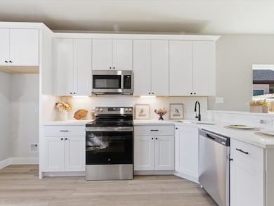 Kitchen featuring appliances with stainless steel finishes, decorative backsplash, white cabinets, and light wood-style flooring