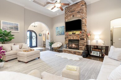 Living room with a stone fireplace, arched walkways, ceiling fan, and wood finished floors