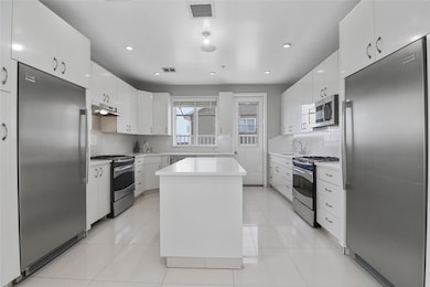 Kitchen with appliances with stainless steel finishes, light countertops, a center island, white cabinetry, and decorative backsplash