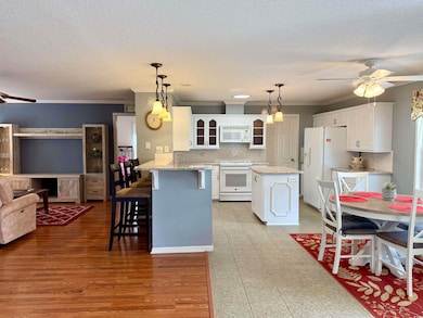 Kitchen with white appliances, ceiling fan, a peninsula, glass insert cabinets, and crown molding