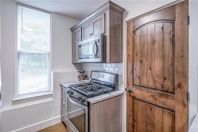 Kitchen featuring appliances with stainless steel finishes, light countertops, backsplash, and baseboards