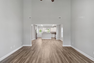 Unfurnished living room featuring dark hardwood / wood-style flooring, ceiling fan, and a towering ceiling