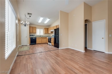 Kitchen with light wood-type flooring, black appliances, open floor plan, light countertops, and hanging light fixtures
