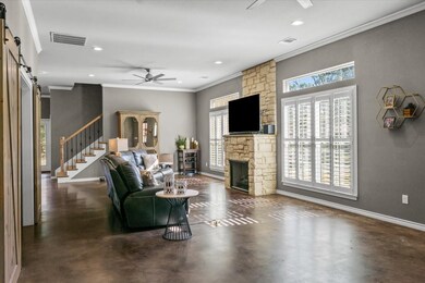Living area with crown molding, ceiling fan, a barn door, concrete floors, and a stone fireplace