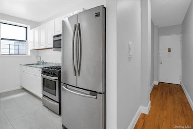 Kitchen with sink, appliances with stainless steel finishes, white cabinets, and light hardwood / wood-style floors