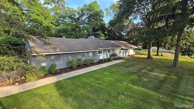 Ranch-style home with a front lawn, a chimney, view of wooded area, and a shingled roof
