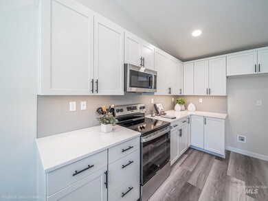 Kitchen with appliances with stainless steel finishes, tasteful backsplash, white cabinetry, light countertops, and light wood finished floors
