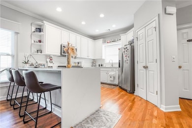 Kitchen with open shelves, white cabinetry, a peninsula, a kitchen breakfast bar, and light wood finished floors