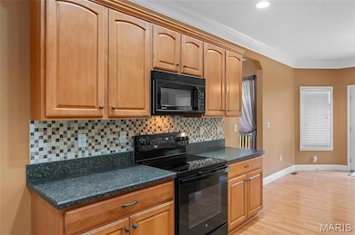 Kitchen with black appliances, backsplash, dark countertops, light wood-type flooring, and ornamental molding