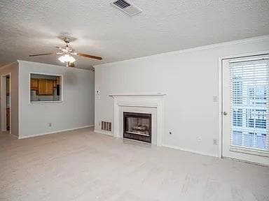 Unfurnished living room with a textured ceiling, a fireplace, crown molding, a ceiling fan, and light colored carpet