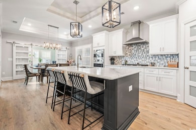 Kitchen featuring a tray ceiling, hanging light fixtures, a barn door, a kitchen breakfast bar, and an island with sink