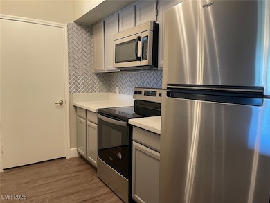 Kitchen featuring gray cabinetry, stainless steel appliances, tasteful backsplash, and dark wood-style floors