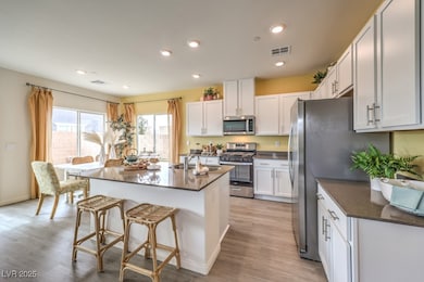 Kitchen featuring appliances with stainless steel finishes, a kitchen bar, a kitchen island with sink, light wood-style floors, and dark stone counters. Home is representational only; actual home finishes may vary.