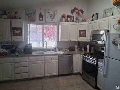 Kitchen featuring a sink, light tile patterned floors, stainless steel appliances, and white cabinetry