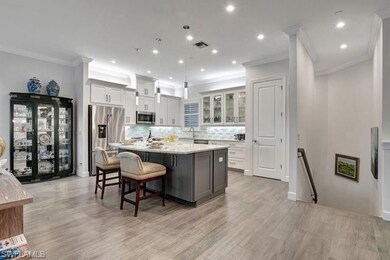 Featuring a large island with seating, hanging pending light fixtures, stainless steel appliances, and cabs with glass fronts.