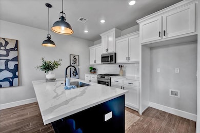 Kitchen with white cabinets, stainless steel appliances, light stone counters, tasteful backsplash, and decorative light fixtures