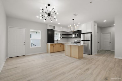 Kitchen featuring an inviting chandelier, open shelves, a kitchen island, appliances with stainless steel finishes, and baseboards