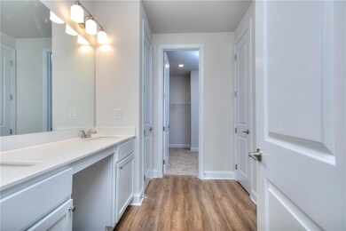 Full bathroom with double vanity, wood-style finished floors, and baseboards