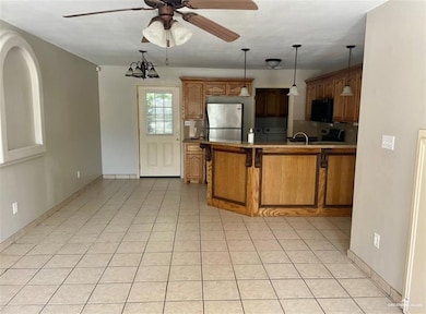 Kitchen with appliances with stainless steel finishes, ceiling fan, a peninsula, brown cabinetry, and decorative light fixtures