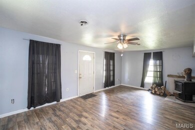 Unfurnished living room with a ceiling fan, a wood stove, wood finished floors, and a textured ceiling