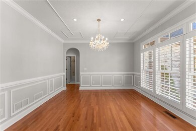 Unfurnished dining area featuring arched walkways, plenty of natural light, a chandelier, light wood finished floors, and a wainscoted wall