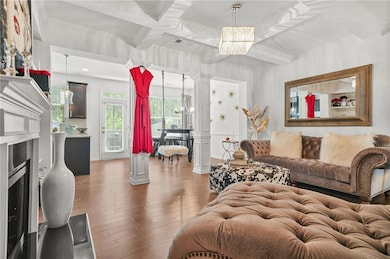 Living area with a chandelier, decorative columns, wood finished floors, coffered ceiling, and ornamental molding