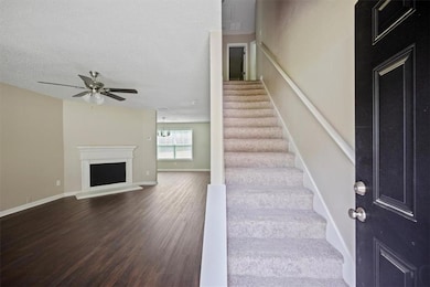 Staircase with wood finished floors, ceiling fan, a fireplace with raised hearth, baseboards, and a textured ceiling