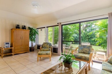 Large living room with tiled floors that opens to a beautiful lanai in a lush garden setting.