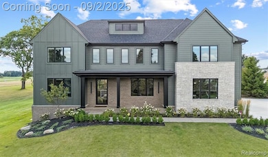 View of front facade with a front lawn, covered porch, a shingled roof, stone siding, and board and batten siding