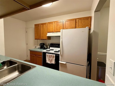 Kitchen with white appliances, brown cabinetry, under cabinet range hood, and light countertops
