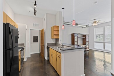 Kitchen featuring finished concrete floors, dark stone countertops, freestanding refrigerator, light brown cabinets, and pendant lighting