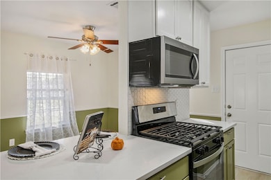 Kitchen featuring stainless steel appliances, light stone counters, backsplash, ceiling fan, and green cabinetry
