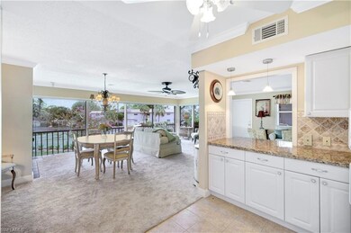 Kitchen featuring pendant lighting, white cabinetry, light stone counters, decorative backsplash, and ornamental molding