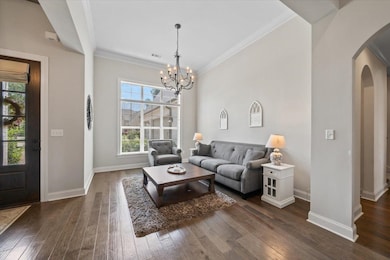 Living room featuring arched walkways, dark wood-type flooring, a chandelier, and ornamental molding