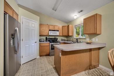 Kitchen with appliances with stainless steel finishes, a peninsula, brown cabinets, light countertops, and lofted ceiling
