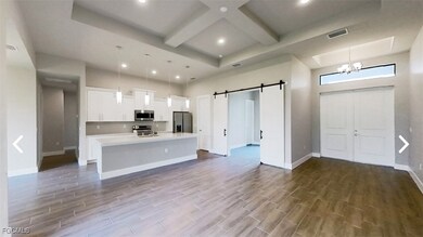 Kitchen featuring open floor plan, a barn door, white cabinets, a kitchen island with sink, and appliances with stainless steel finishes