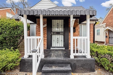 View of exterior entry with brick siding, a porch, and roof with shingles