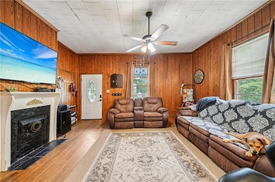 Living room with wooden walls, ceiling fan, a fireplace with flush hearth, wood finished floors, and crown molding
