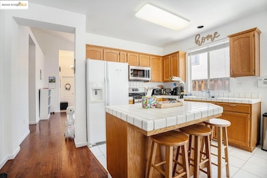 Kitchen featuring appliances with stainless steel finishes, a center island, tile countertops, light wood-type flooring, and a kitchen breakfast bar