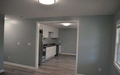 Kitchen with appliances with stainless steel finishes, baseboards, dark wood-type flooring, and dark countertops