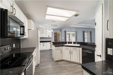 Kitchen featuring black appliances, a sink, a chandelier, white cabinets, and light wood-style floors