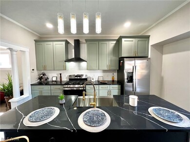 Kitchen with sink, appliances with stainless steel finishes, ornate columns, wall chimney exhaust hood, and decorative light fixtures