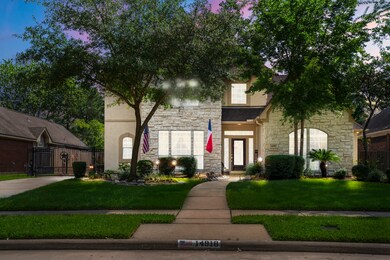A two-story suburban house at dusk, with stone and stucco facade, manicured lawn illuminated by exterior lights.