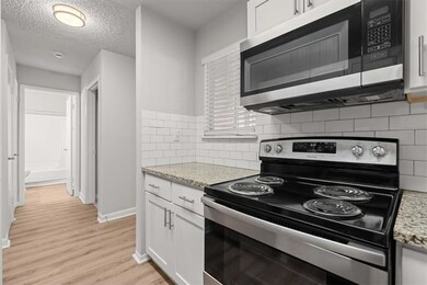 Kitchen with light wood-type flooring, baseboards, decorative backsplash, appliances with stainless steel finishes, and white cabinetry
