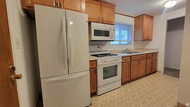 Kitchen featuring white appliances, light countertops, light flooring, brown cabinets, and crown molding