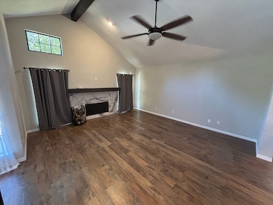 Unfurnished living room featuring dark wood-style floors, beam ceiling, a fireplace, high vaulted ceiling, and ceiling fan