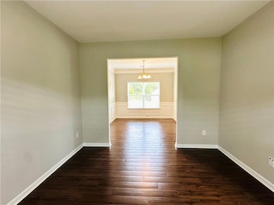 Empty room featuring a chandelier, dark wood-type flooring, crown molding, and baseboards