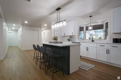 Kitchen with white cabinetry, a breakfast bar, decorative light fixtures, a textured ceiling, and recessed lighting