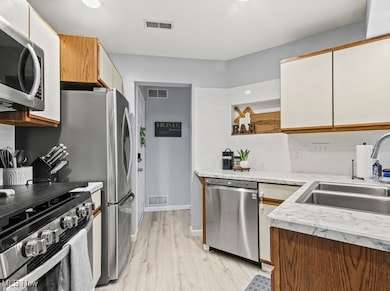 Kitchen with light countertops, appliances with stainless steel finishes, light wood-style flooring, white cabinetry, and brown cabinets