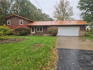 View of front facade featuring brick siding, concrete driveway, a metal roof, a front lawn, and a garage